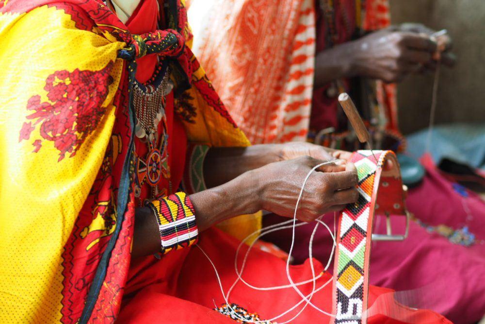 Maasai women in traditional clothing making handicrafts.