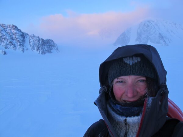 Woman in snowsuit standing in front of arctic mountains.