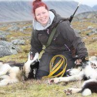 Woman sitting on grass playing with husky dogs on Svalbard.