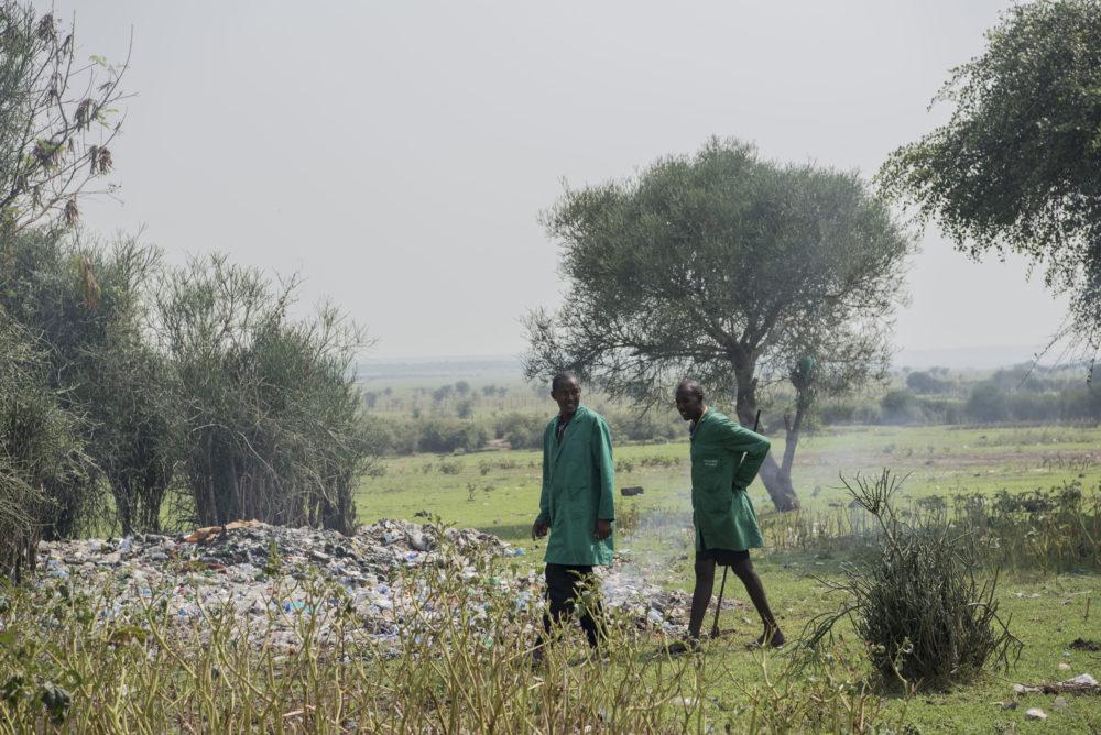 Two men walking in field littered with waste and plastic in Kenya.