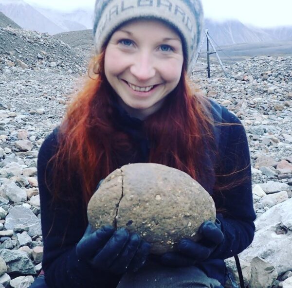 Woman holding rock and smiling into camera at wharf on Svalbard.