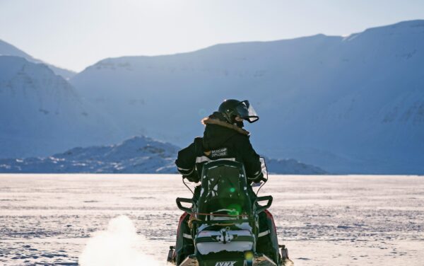 Person in Basecamp Explorer snowsuit with helmet driving a snowmobile in Spitsbergen.